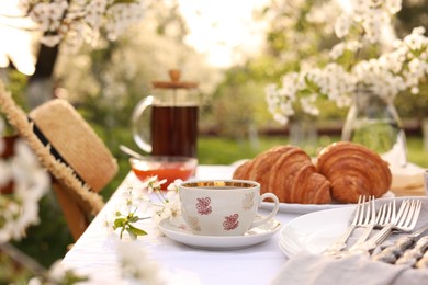 Stylish table setting with beautiful spring flowers, tea and croissants in garden