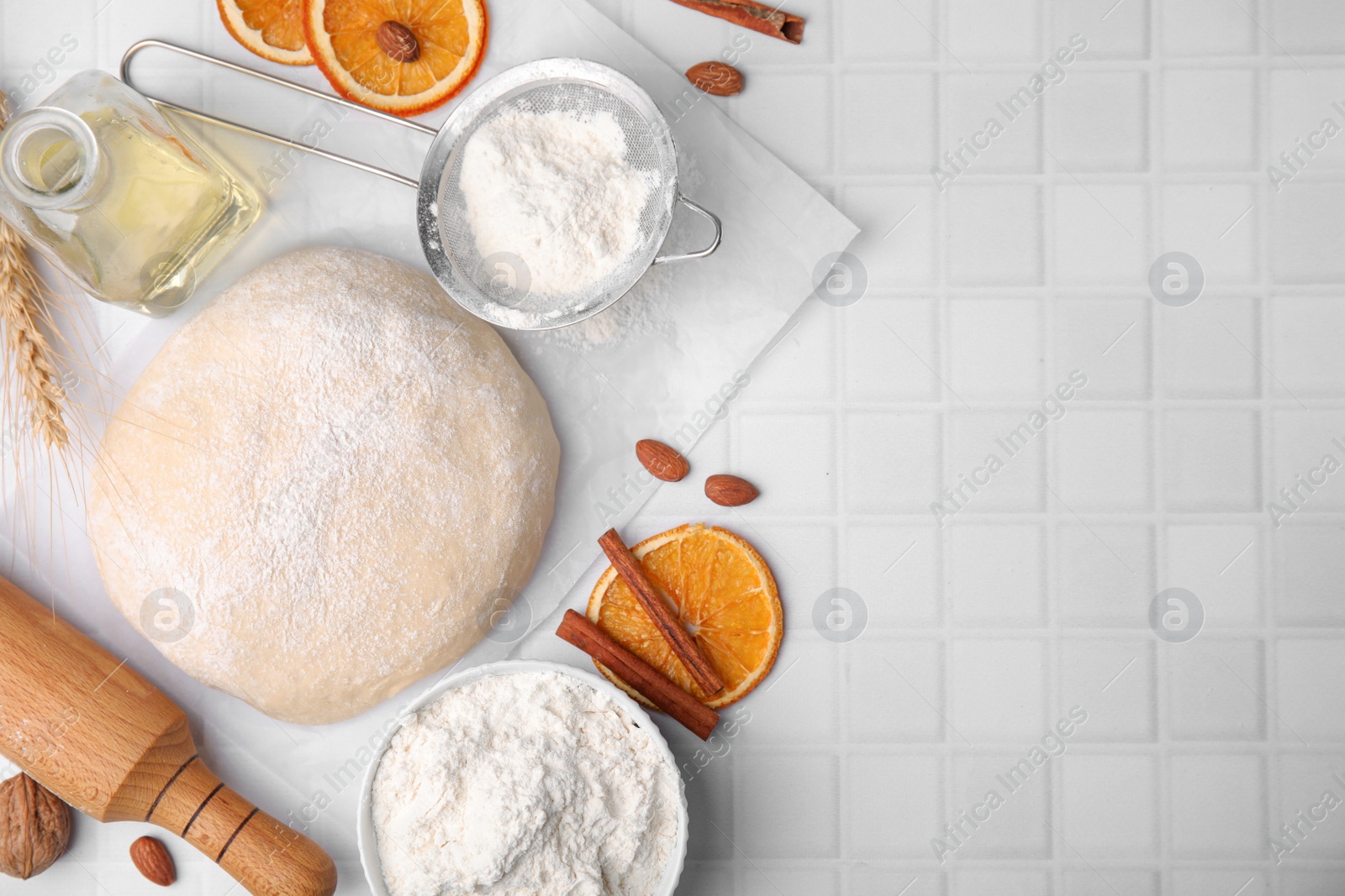 Photo of Fresh dough and other ingredients on white tiled table, flat lay. Space for text