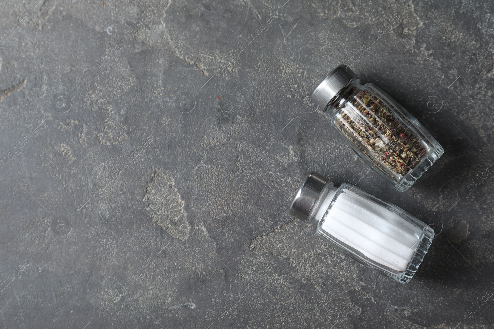 Photo of Salt and pepper shakers on grey textured table, top view. Space for text