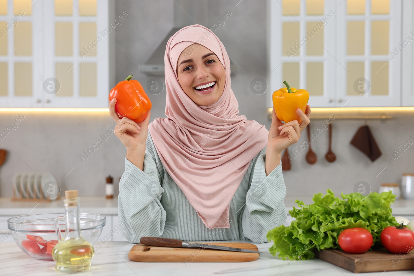 Photo of Muslim woman making delicious salad with vegetables at white table in kitchen