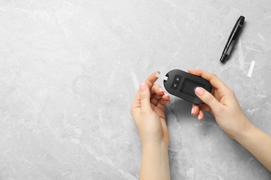 Photo of Diabetes. Woman checking blood sugar level with glucometer at gray marble table, top view. Space for text