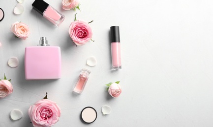 Flat lay composition with bottles of perfume, cosmetics and roses on grey background. Space for text