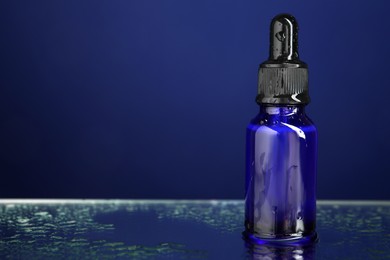 Photo of Bottle of face serum on wet surface against blue background, closeup. Space for text
