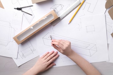 Woman creating packaging design at light wooden table, top view