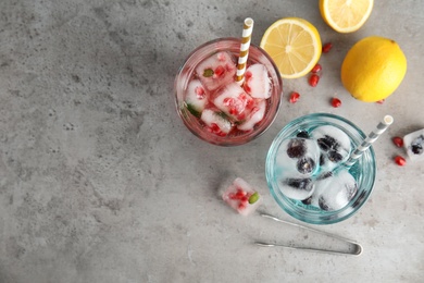 Photo of Tasty cocktails with fruit ice cubes and lemons on grey background, top view. Space for text