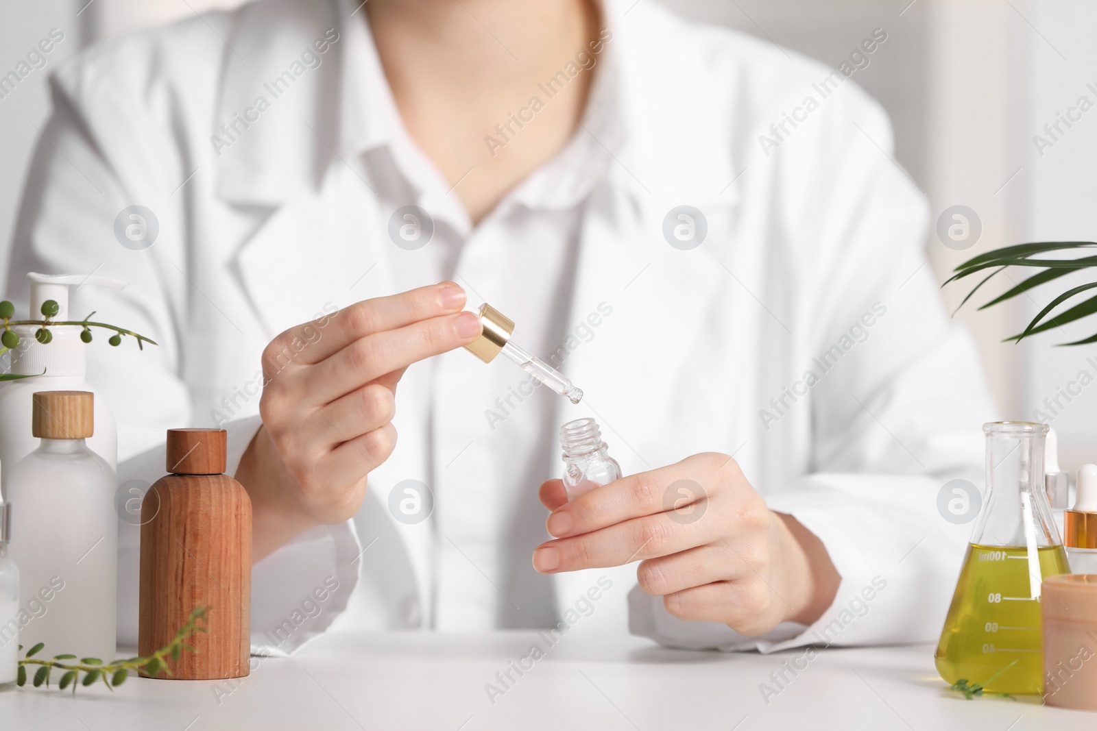 Photo of Dermatologist testing essential oil at white table indoors, selective focus