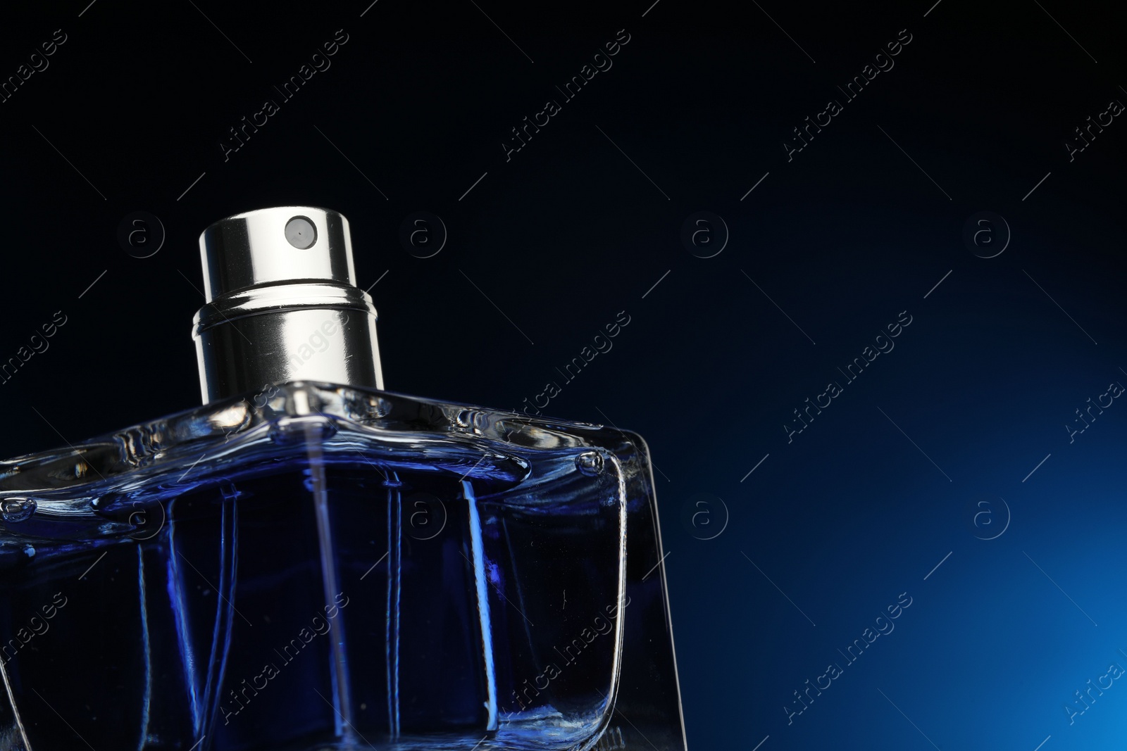 Photo of Luxury men`s perfume in bottle against dark blue background, closeup. Space for text