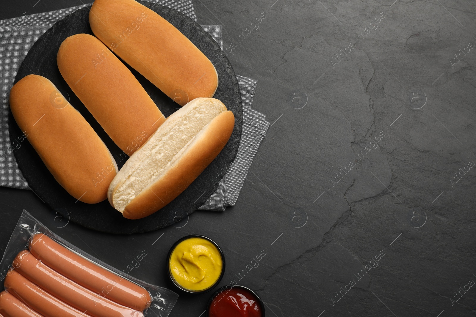 Photo of Different tasty ingredients for hot dog on dark table, flat lay. Space for text