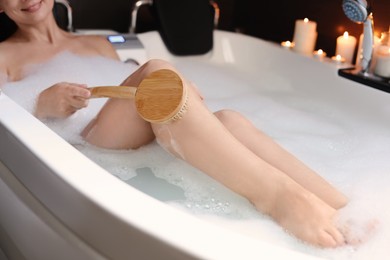 Photo of Woman rubbing leg with brush while taking bubble bath, closeup. Romantic atmosphere