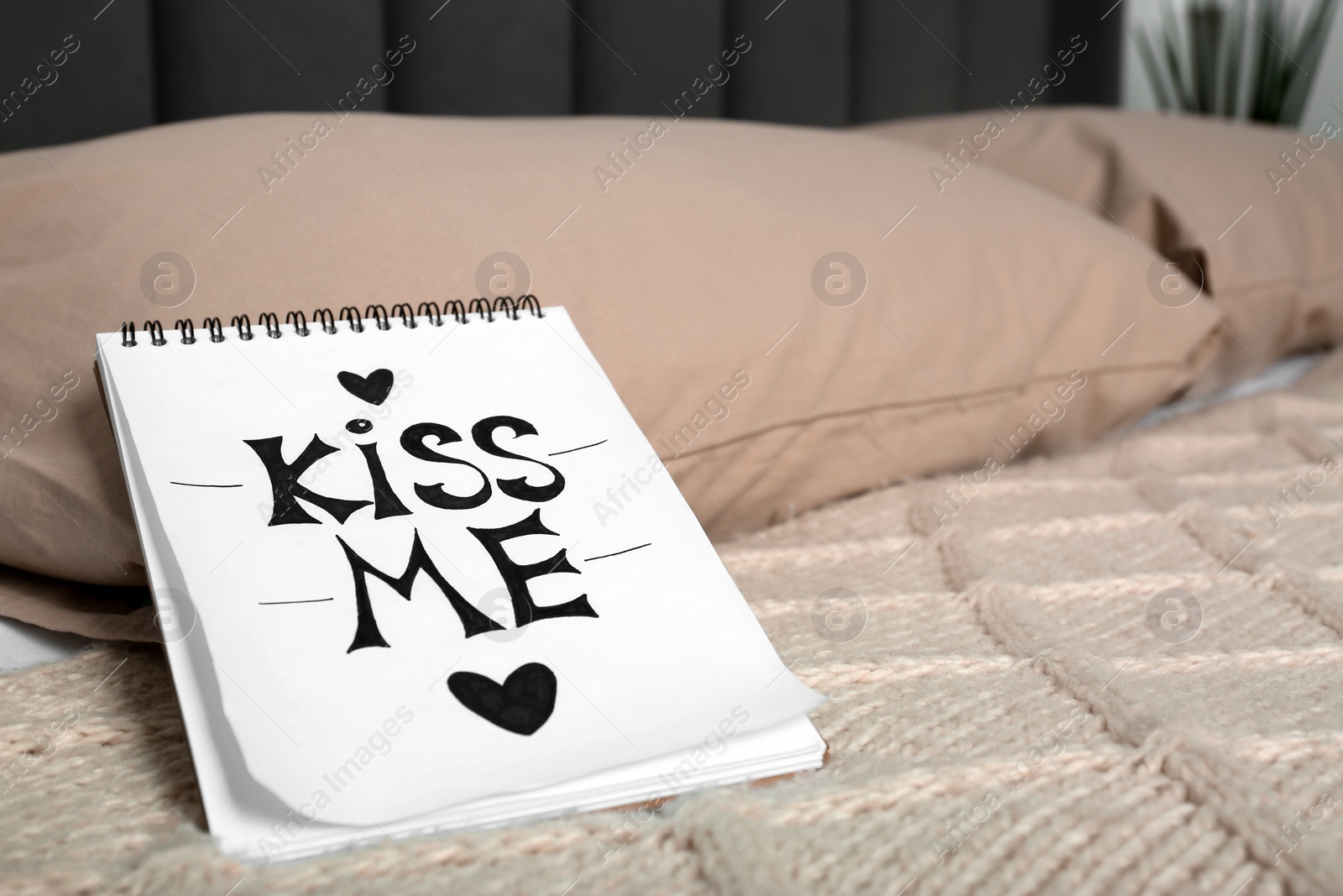 Notebook with phrase Kiss Me and hearts on bed in room, closeup. Space for text Photo of Notebook with phrase Kiss Me and hearts on bed in room, closeup. Space for text