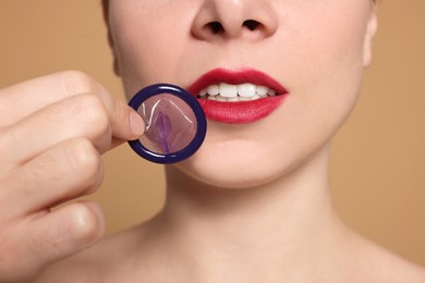 Photo of Woman holding condom on beige background, closeup. Safe sex