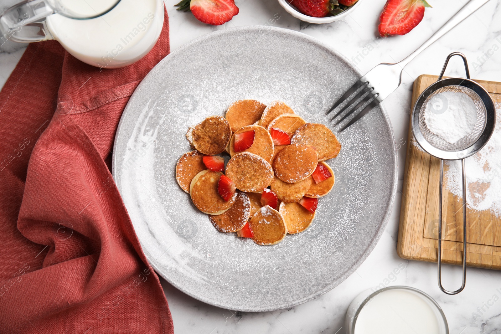 Photo of Delicious mini pancakes cereal with strawberries served on white marble table, flat lay