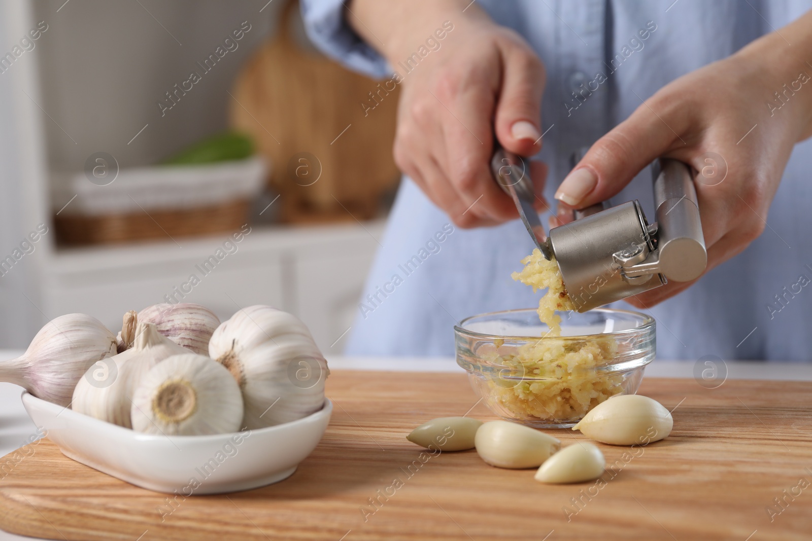 Photo of Woman squeezing garlic with press at wooden table in kitchen, closeup