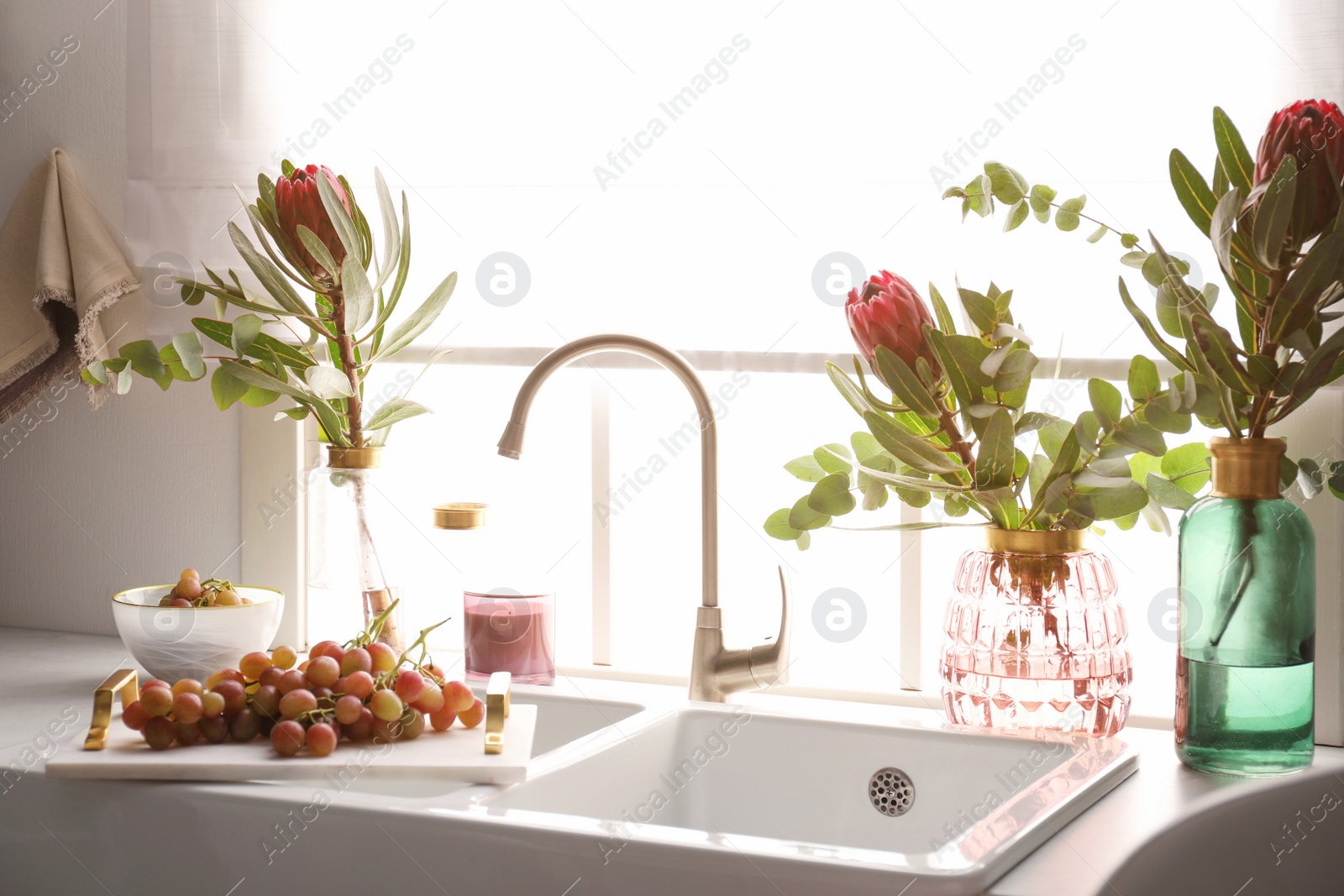 Photo of Vases with beautiful protea flowers near sink in kitchen. Interior design