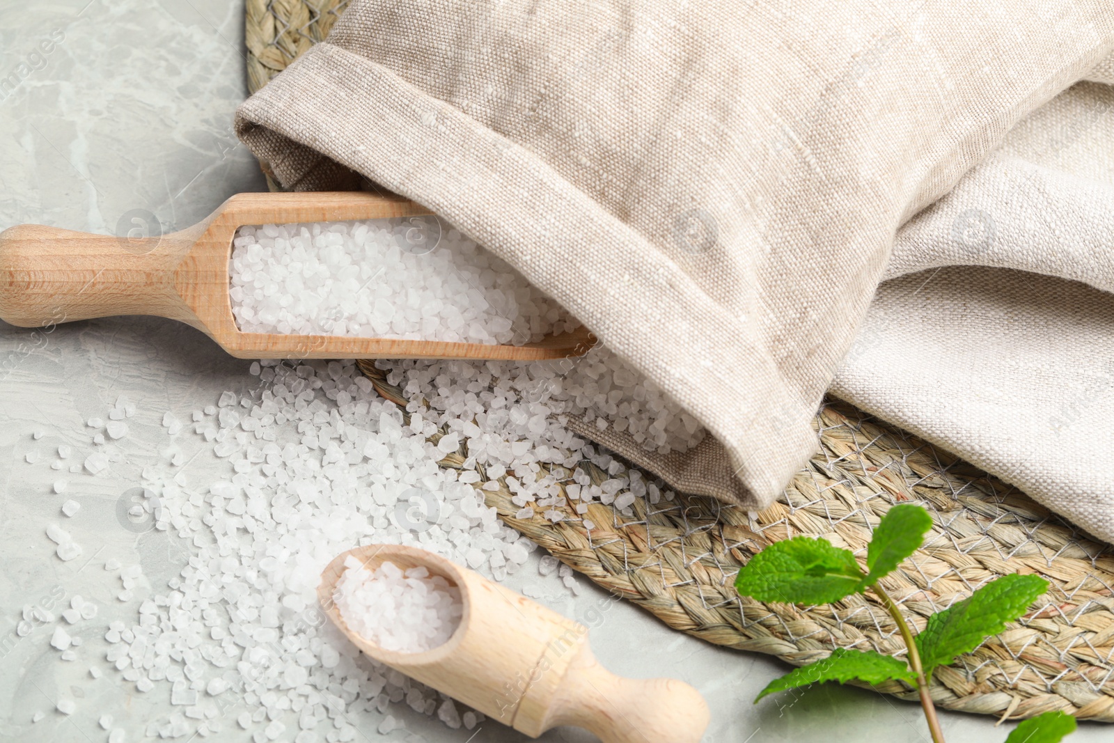 Photo of Wooden scoops with natural sea salt and sack on light grey marble table, closeup