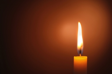 Photo of Wax candle burning in darkness, closeup