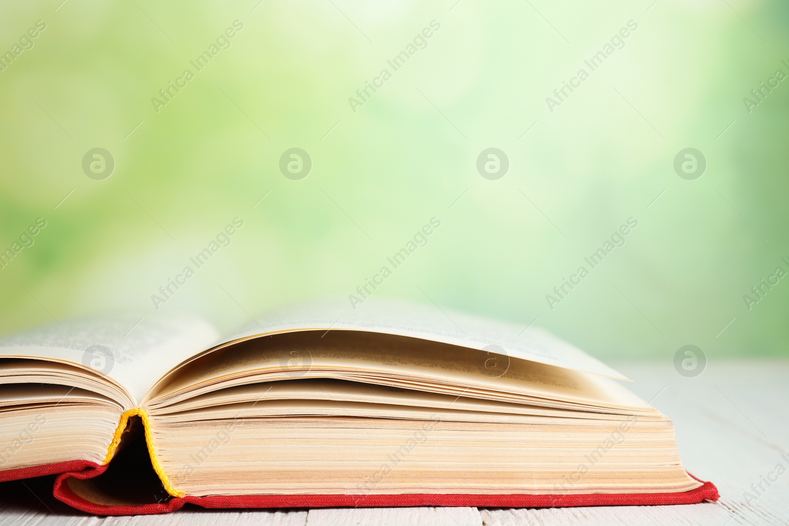 Photo of Open book on white wooden table against blurred green background, closeup. Space for text