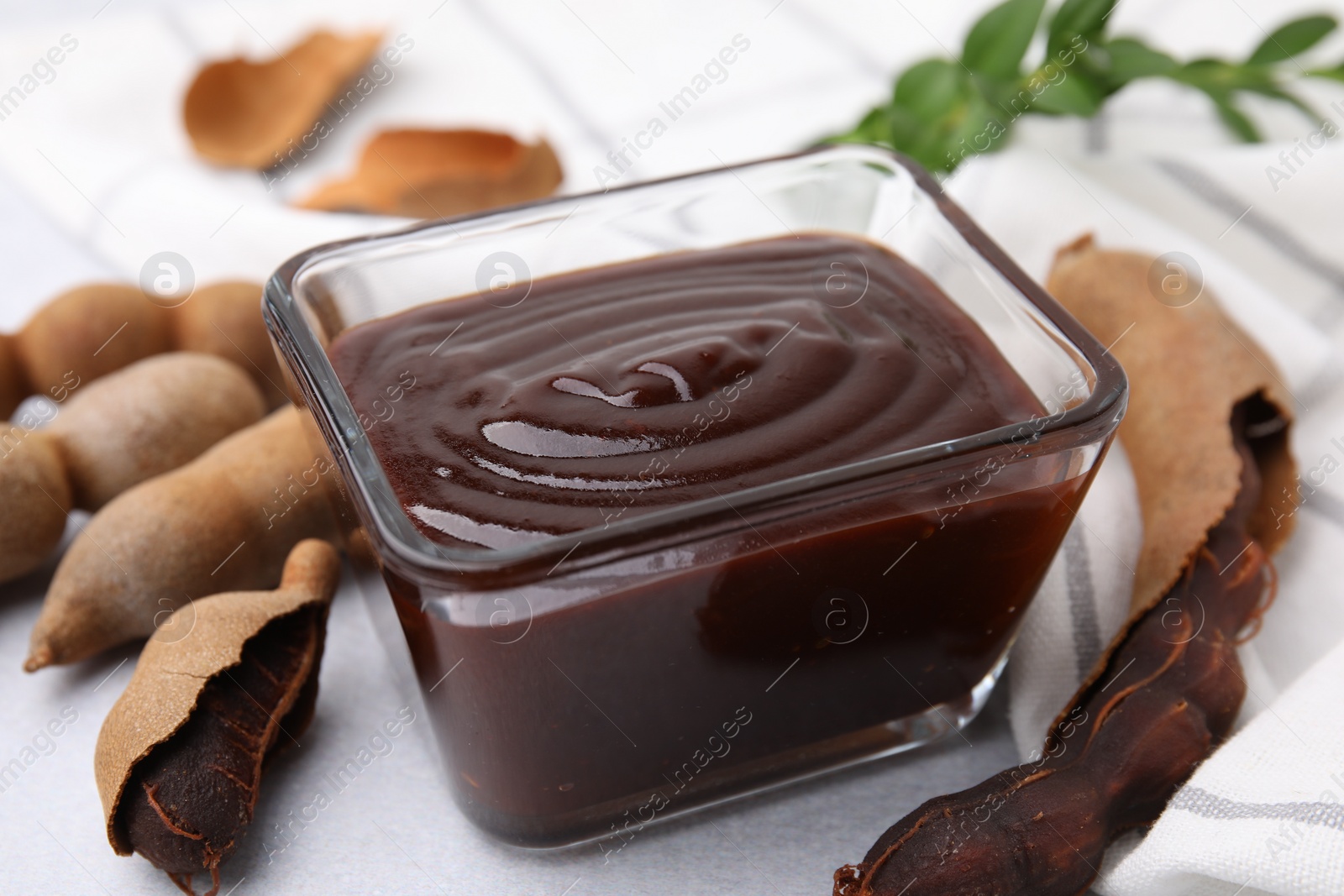 Bowl of tasty tamarind sauce and fresh pods on light table, closeup Photo of Bowl of tasty tamarind sauce and fresh pods on light table, closeup
