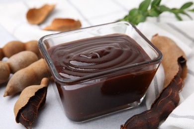 Photo of Bowl of tasty tamarind sauce and fresh pods on light table, closeup
