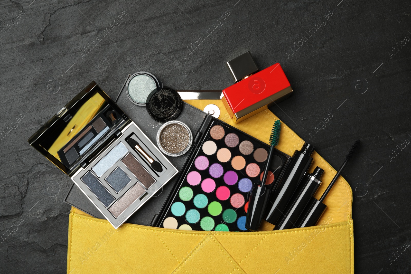 Photo of Cosmetic bag with makeup products on black slate background, flat lay