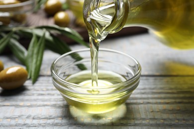 Pouring olive oil into bowl on wooden table, closeup. Healthy cooking