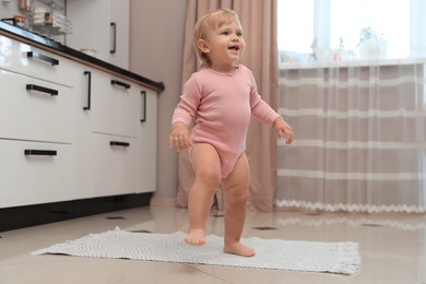 Cute baby learning to walk in kitchen near window