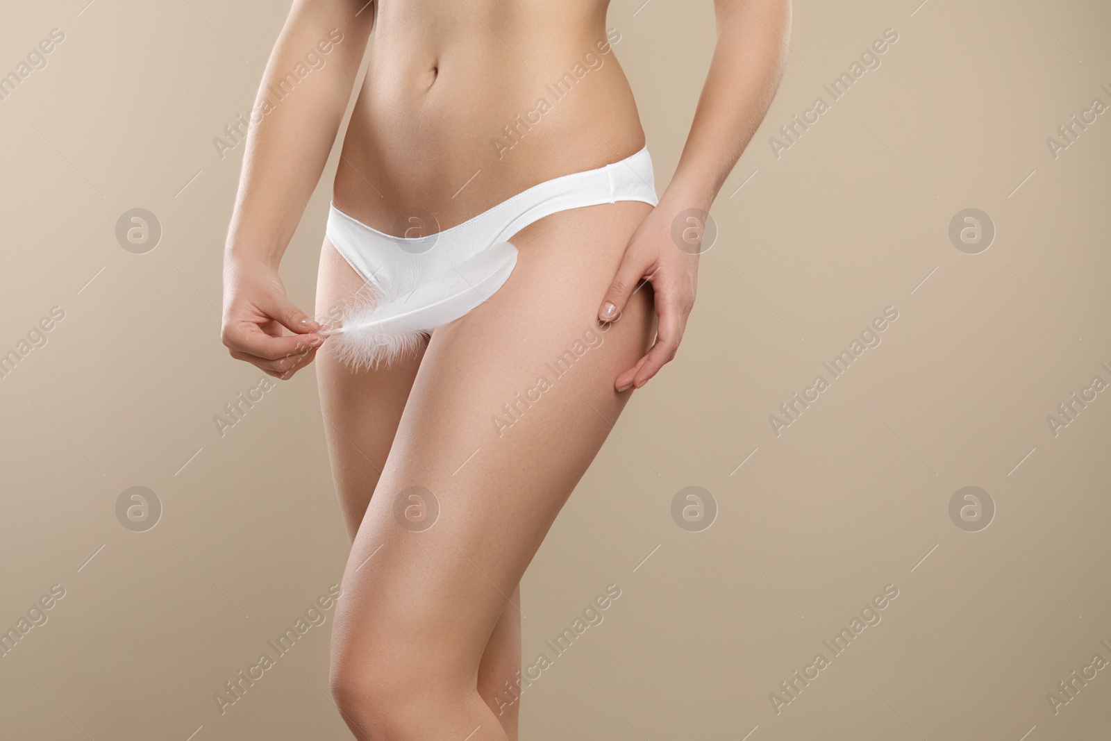 Photo of Woman with feather showing smooth skin on beige background, closeup. Brazilian bikini epilation