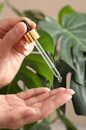 Photo of Woman applying cosmetic serum onto her hand near green plant, closeup