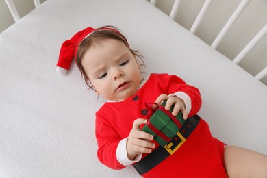 Photo of Cute baby wearing festive Christmas costume with gift box in crib, above view