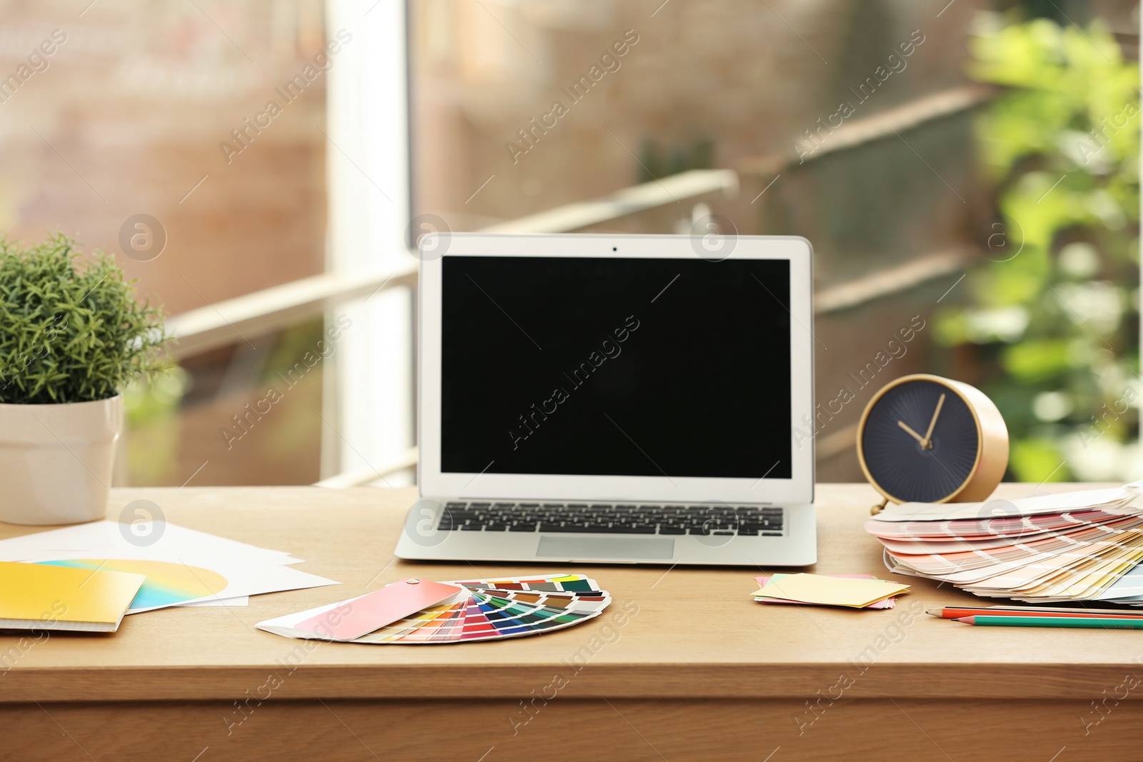 Photo of Designer's workplace with laptop and paint color palette samples on table