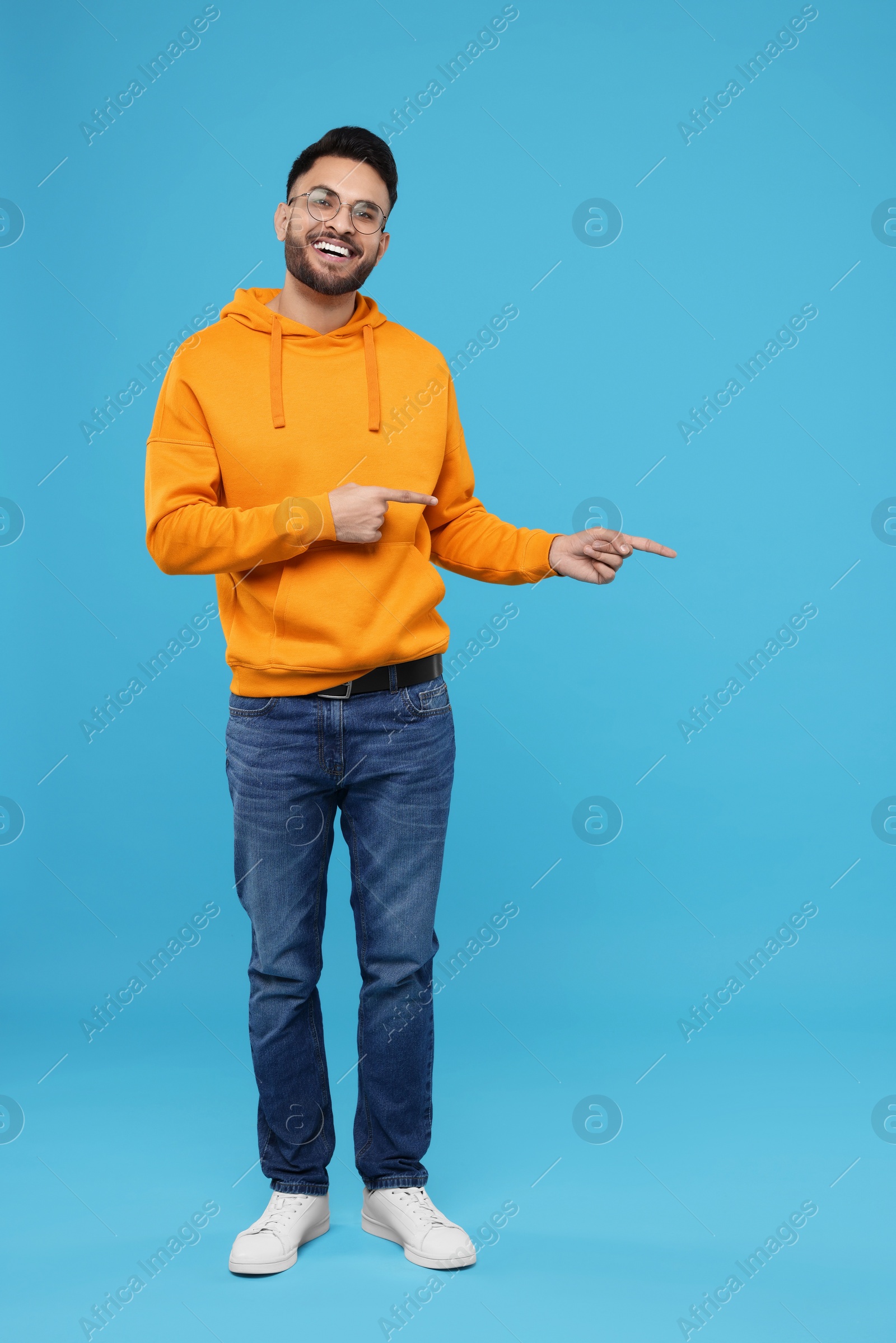 Photo of Happy young man pointing at something on light blue background