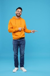 Happy young man pointing at something on light blue background