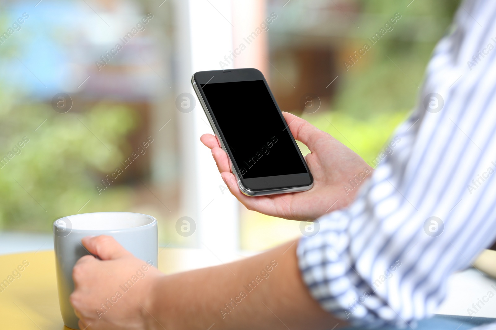 Photo of Woman holding smartphone with blank screen on blurred background. Mockup for design