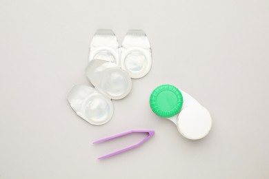 Photo of Packages with contact lenses, case and tweezers on white background, flat lay