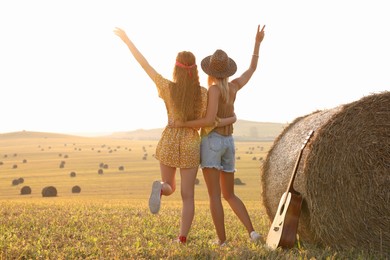 Hippie women near hay bale in field, back view