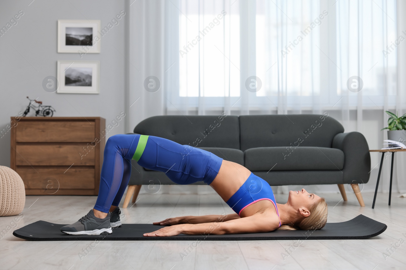 Photo of Athletic woman doing exercise with fitness elastic band on mat at home