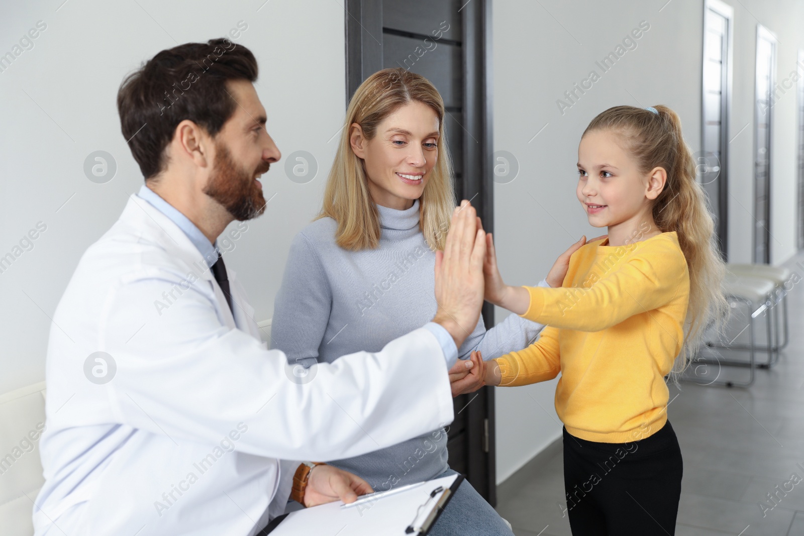 Photo of Happy mother and daughter having appointment with doctor. Pediatrician and patient giving high five in clinic