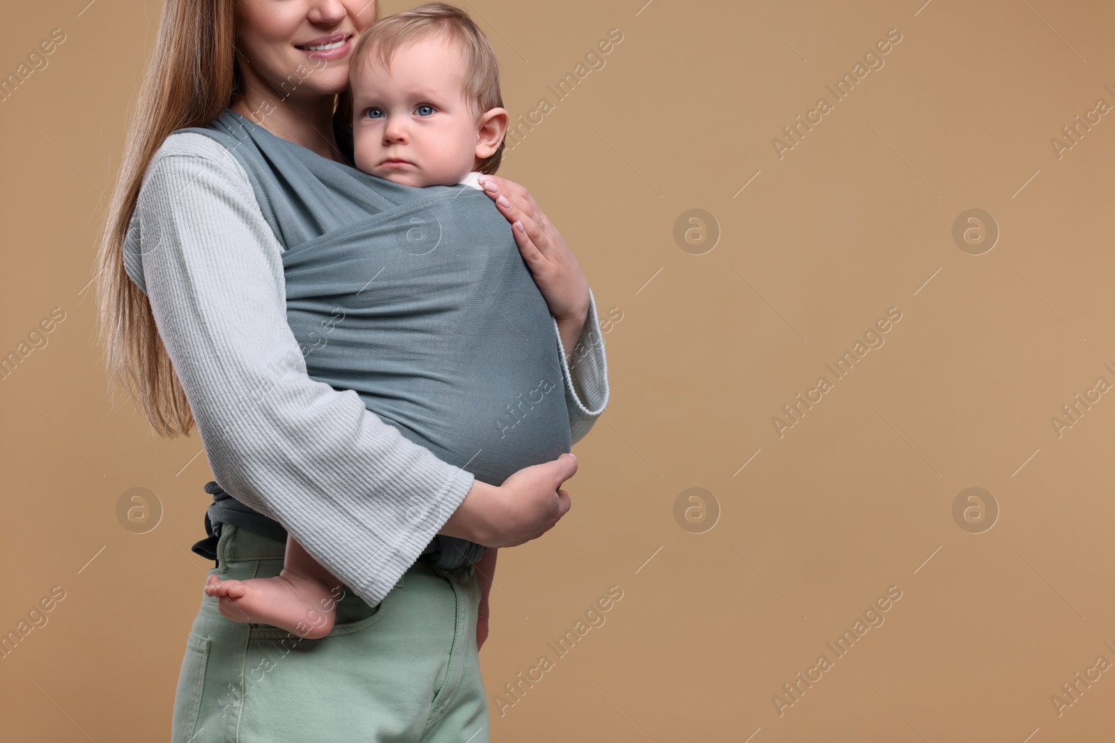 Photo of Mother holding her child in baby wrap on light brown background, closeup. Space for text
