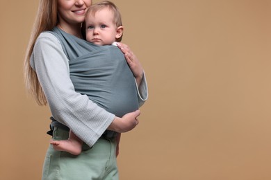 Mother holding her child in baby wrap on light brown background, closeup. Space for text