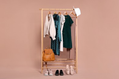 Photo of Rack with accessories and stylish women`s clothes on wooden hangers against beige background