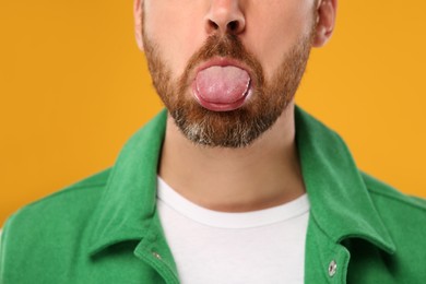 Photo of Man showing his tongue on orange background, closeup