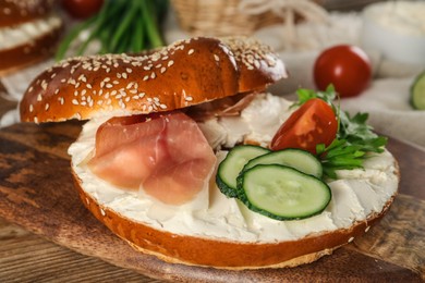 Delicious bagel with cream cheese, jamon, cucumber, tomato and parsley on wooden board, closeup