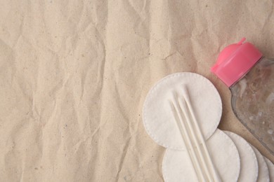 Makeup remover, cotton swabs and pads on crumpled paper, flat lay. Space for text