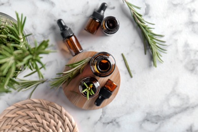 Photo of Bottles with rosemary essential oil on light background, top view