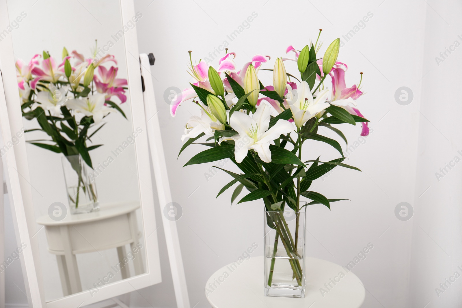 Photo of Vase with bouquet of beautiful lilies on white table near mirror