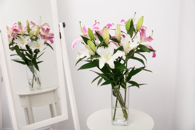 Photo of Vase with bouquet of beautiful lilies on white table near mirror