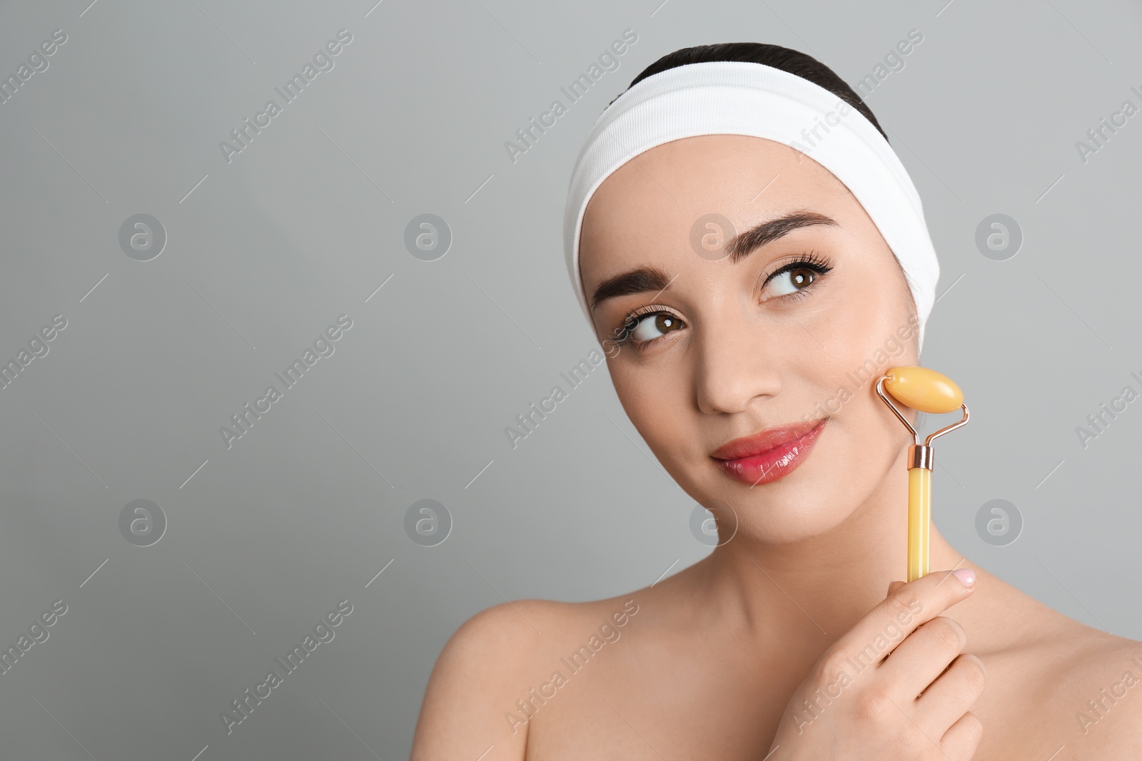 Photo of Woman using natural jade face roller on grey background, space for text