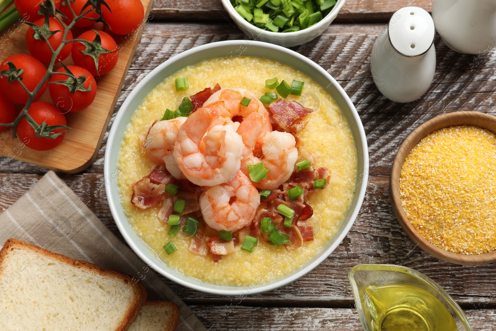 Photo of Fresh tasty shrimps, bacon, grits and green onion in bowl on wooden table, flat lay
