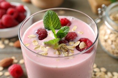 Photo of Glass of tasty raspberry smoothie with oatmeal and mint on table, closeup