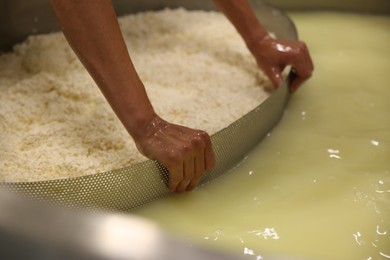 Worker separating curd from whey in tank at cheese factory, closeup